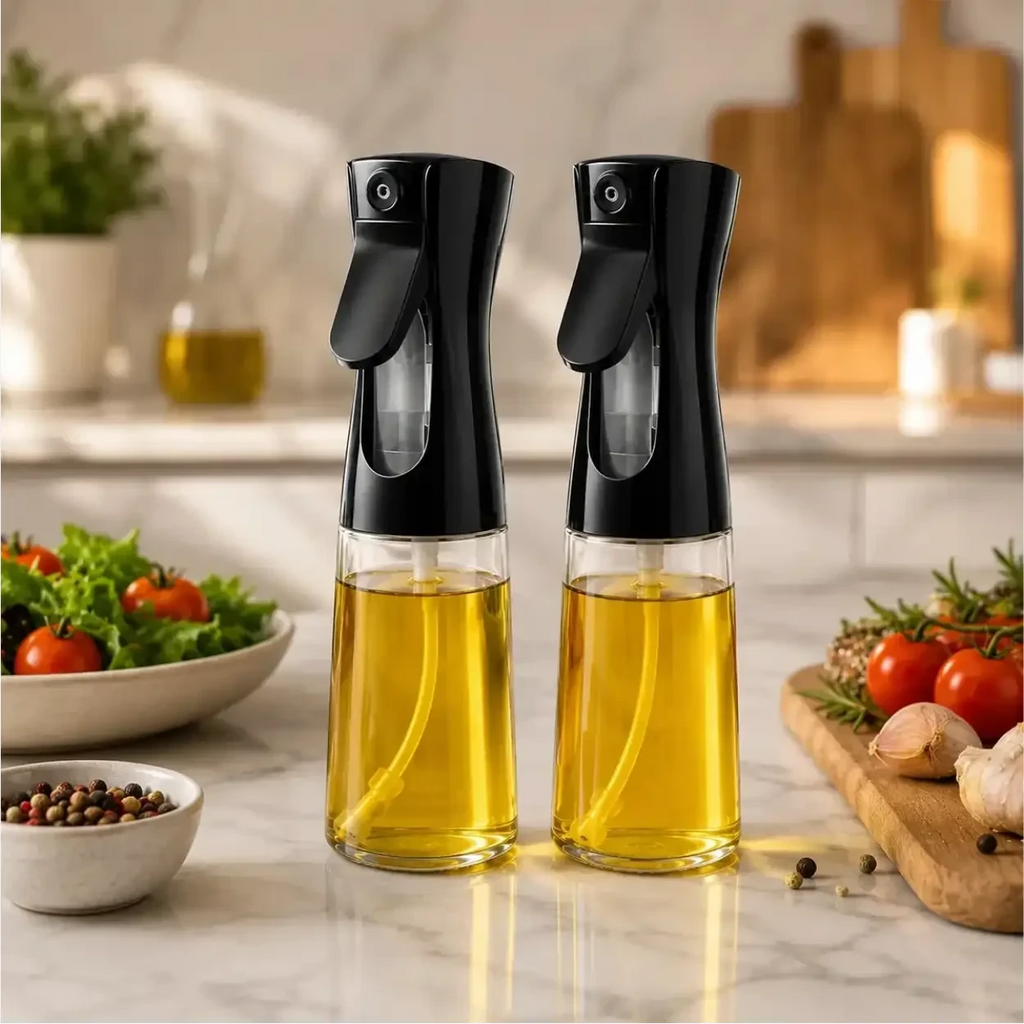 Dois borrifadores de óleo Decoricasa com base de vidro e gatilho preto em bancada de cozinha com vegetais ao fundo