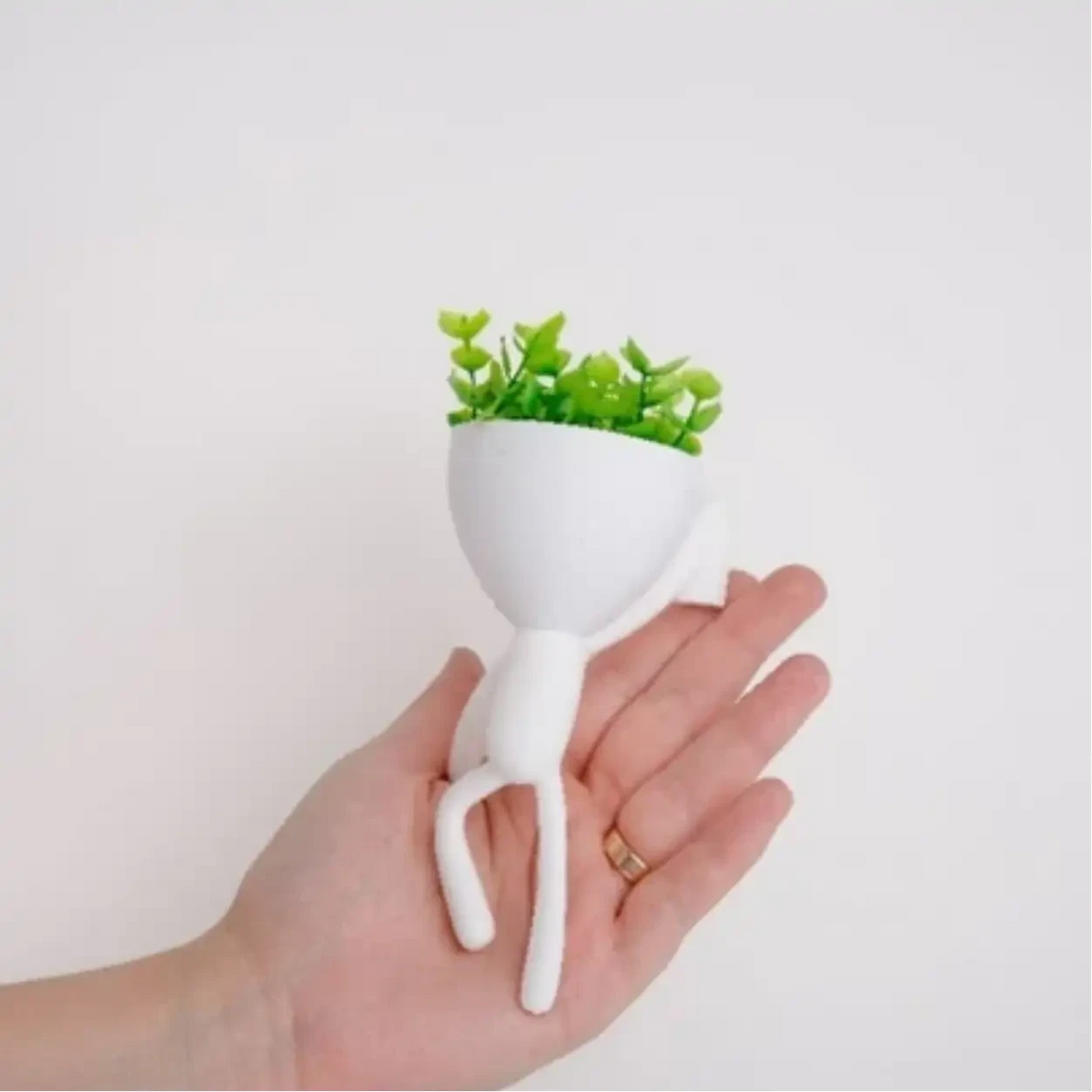Mini vaso alpinista Decoricasa branco com planta artificial verde sendo segurado na palma da mão