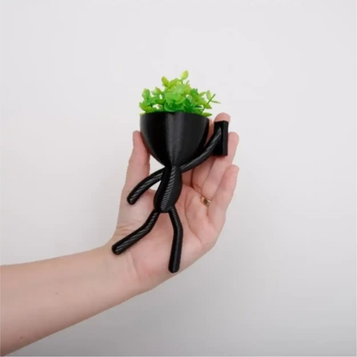 Mini vaso alpinista Decoricasa preto em formato de boneco segurando planta artificial verde na palma da mão