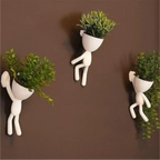 Kit com 3 mini vasos Decoricasa em formato de alpinistas brancos com plantas artificiais fixados em parede marrom