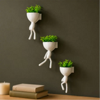 Kit com 3 mini vasos Decoricasa em formato de alpinistas brancos com plantas artificiais verdes em parede escura