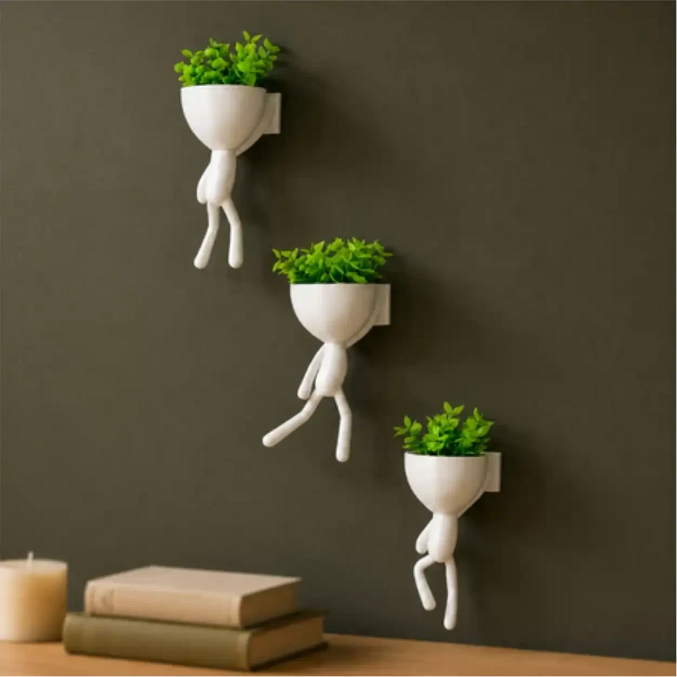 Kit com 3 mini vasos Decoricasa em formato de alpinistas brancos com plantas artificiais verdes em parede escura