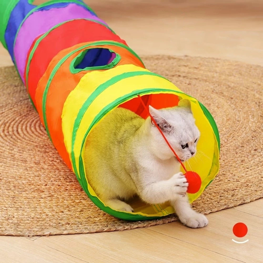 Gato branco brincando com bolinha em túnel labirinto colorido e dobrável da Decoricasa sobre tapete de fibra natural.
